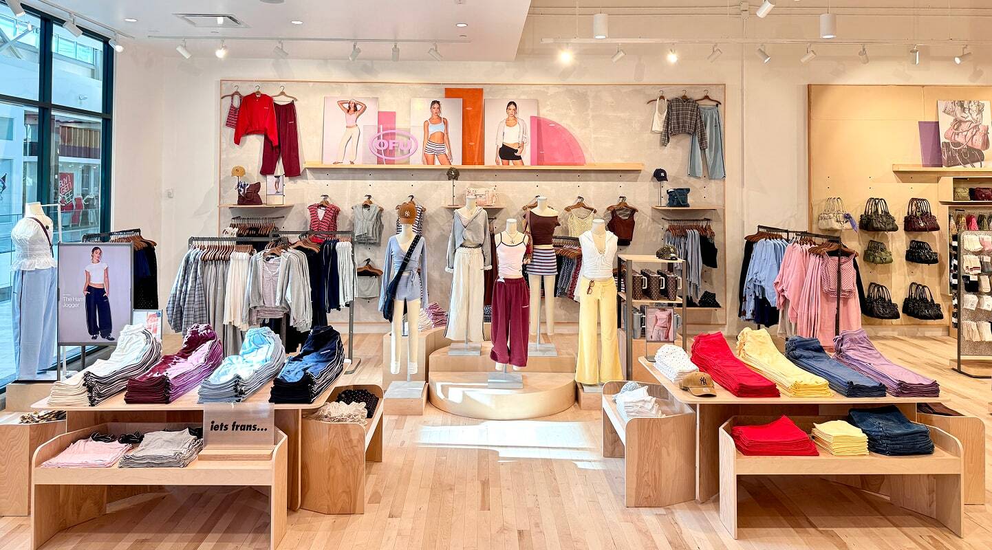 Modern retail clothing store interior with colorful apparel displays, wooden fixtures, mannequins, and bright lighting.