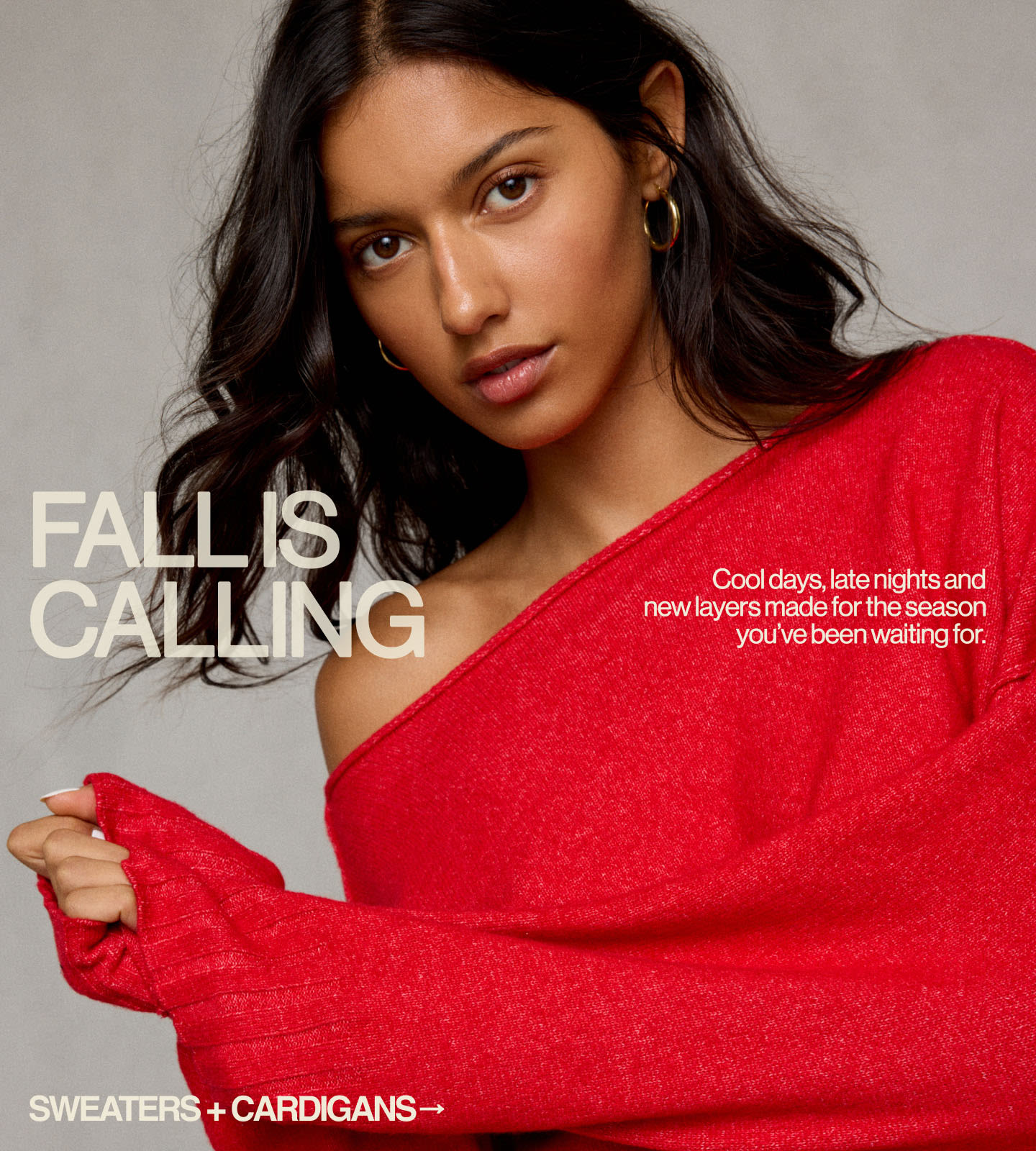 Woman with long dark hair wearing a bright red sweater and gold hoop earrings against a neutral background.