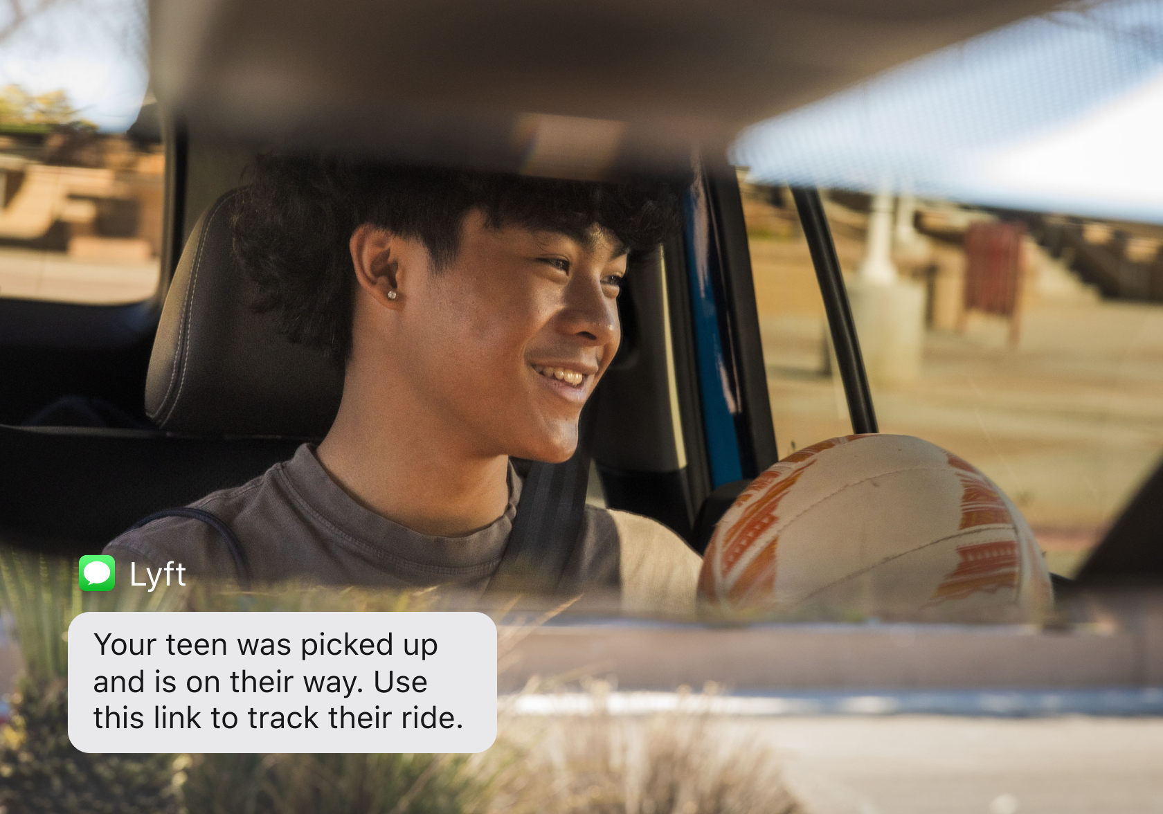 Smiling teen in a car holding a soccer ball, with a Lyft pickup text notification overlay.