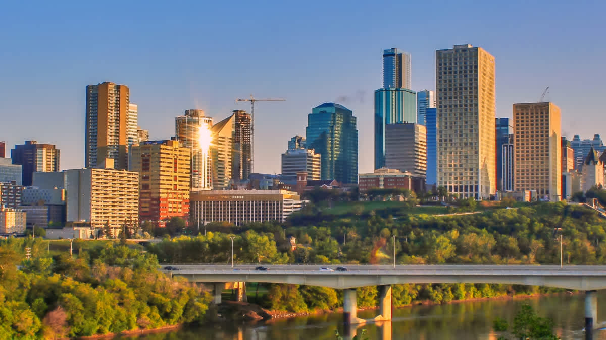 Edmonton city skyline with tall buildings, a bridge over a river, and green trees under a clear blue sky.