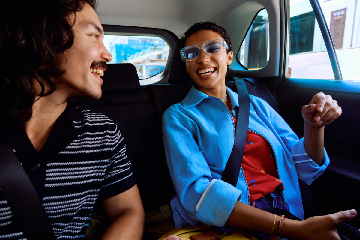Image of smiling driver looking back at a smiling passenger in a car.