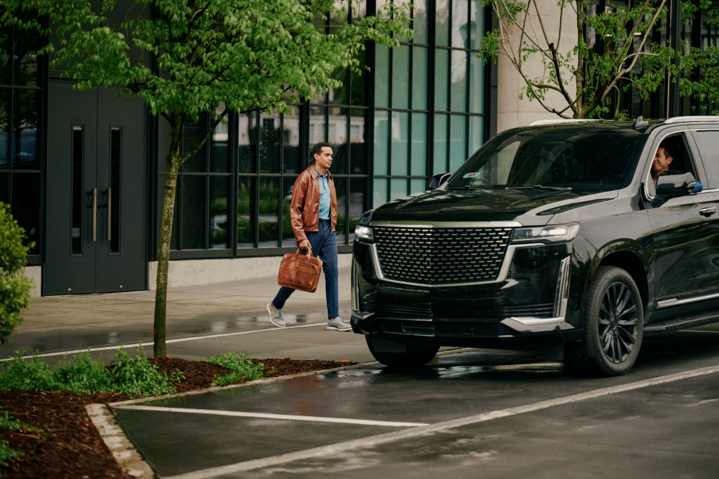 Man with brown briefcase walks past black SUV outside modern glass building