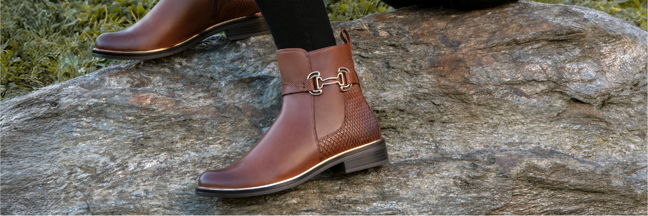 Bottes de Chelsea marron avec boucle dorée sur un rocher, herbe verte en arrière-plan