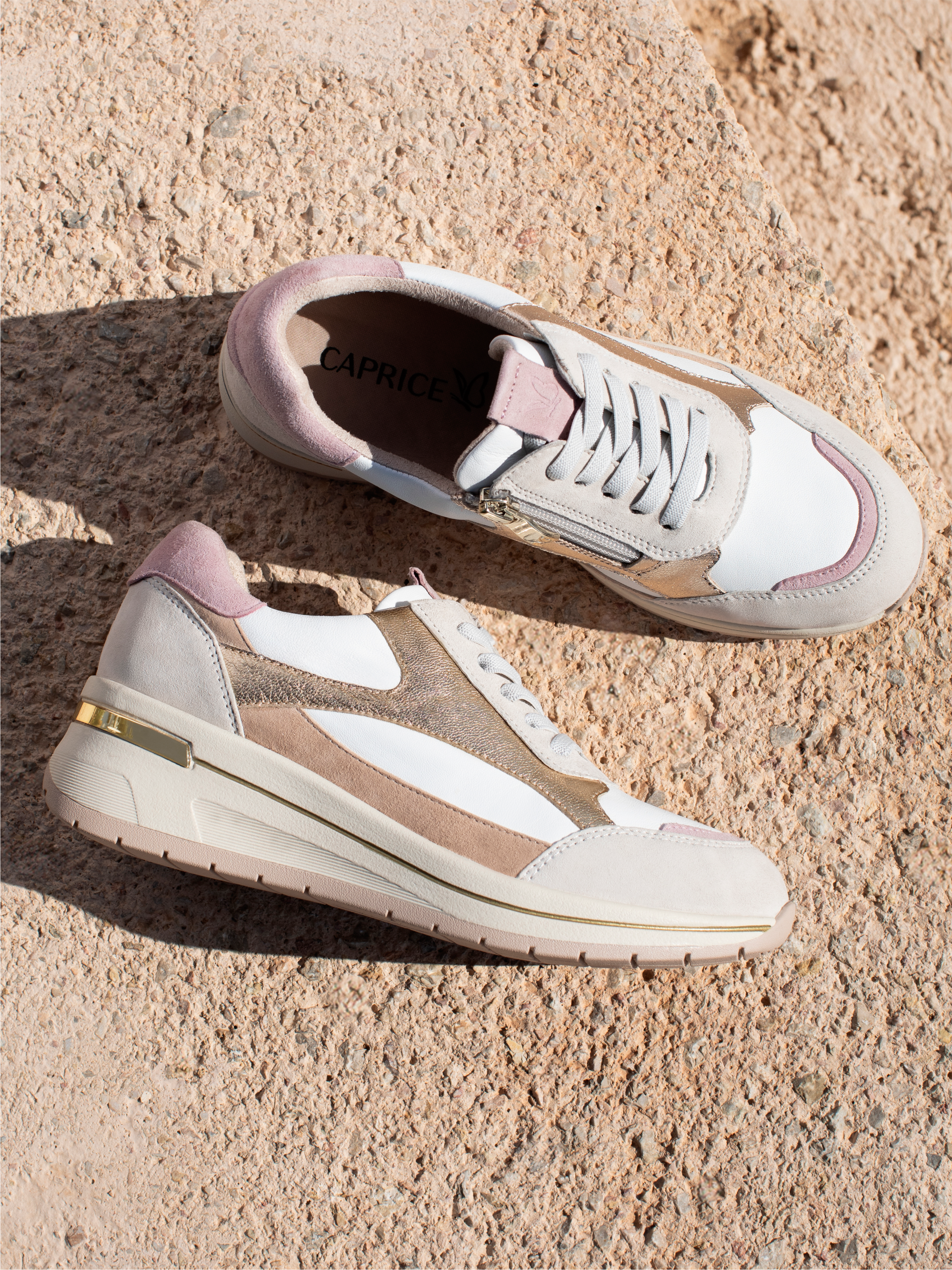 Scarpe da ginnastica bianche con accenti rosa e beige su uno sfondo color sabbia con ombreggiatura