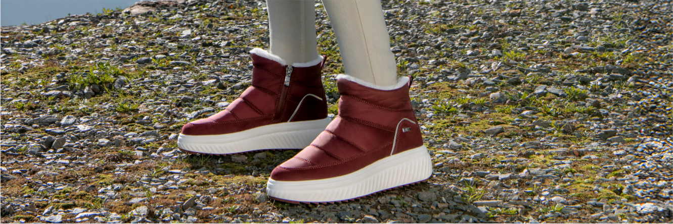 Bottes d'hiver fourrées rouge bordeaux avec semelle blanche sur sol pierreux avec mousse