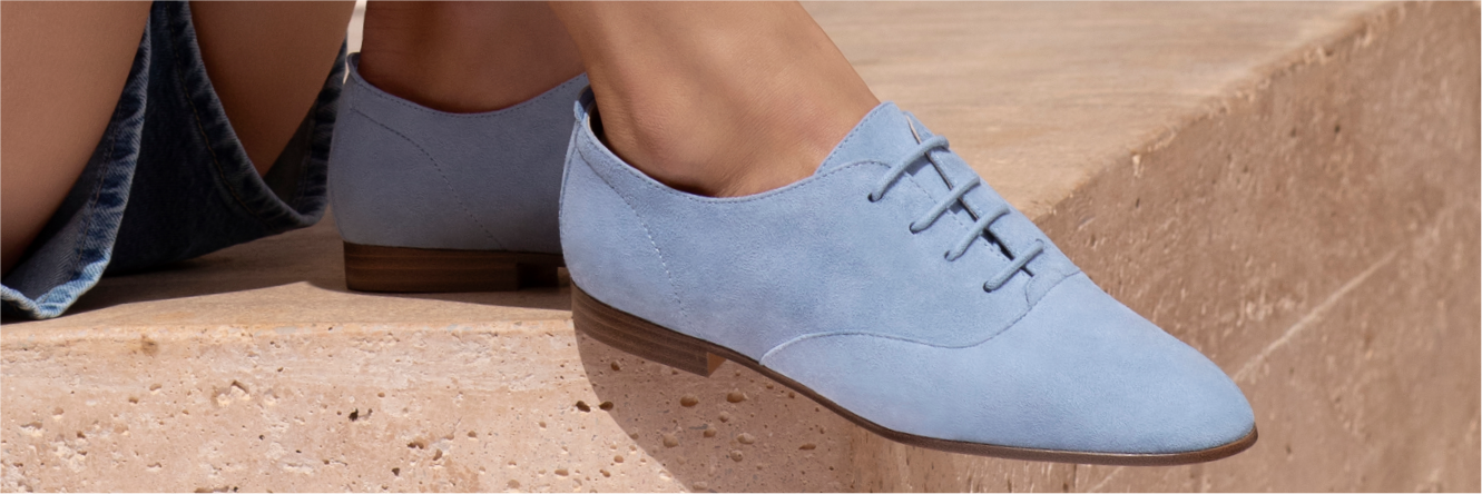 Gros plan sur des chaussures à lacets en daim bleu clair avec un talon marron, portées sur un escalier en pierre à l'extérieur