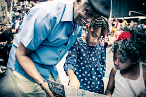 An older man smiles and shows something in a booklet to two younger girls.