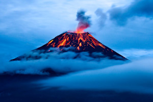 A faraway shot of an active volcano with smoke billowing from the top.