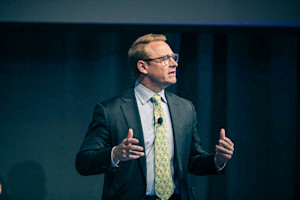 Man in a suit and tie with glasses speaking.