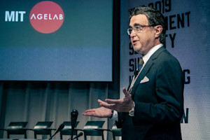 Man stands in front of microphones with a screen in the background.