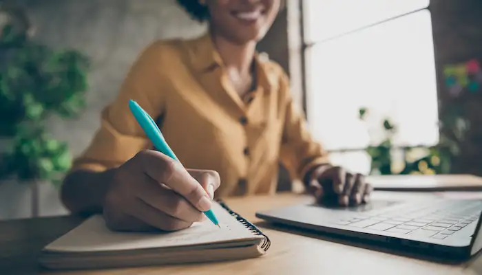 women sat at a desk writing in a notebook