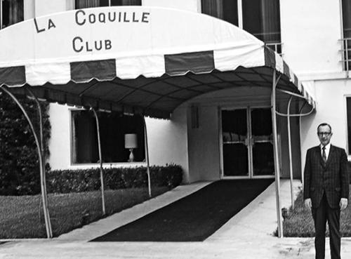 Vintage black and white photograph of a man standing in front of La Coquille Club.