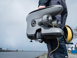 Person holding X3 with DVL and tether reel by the river