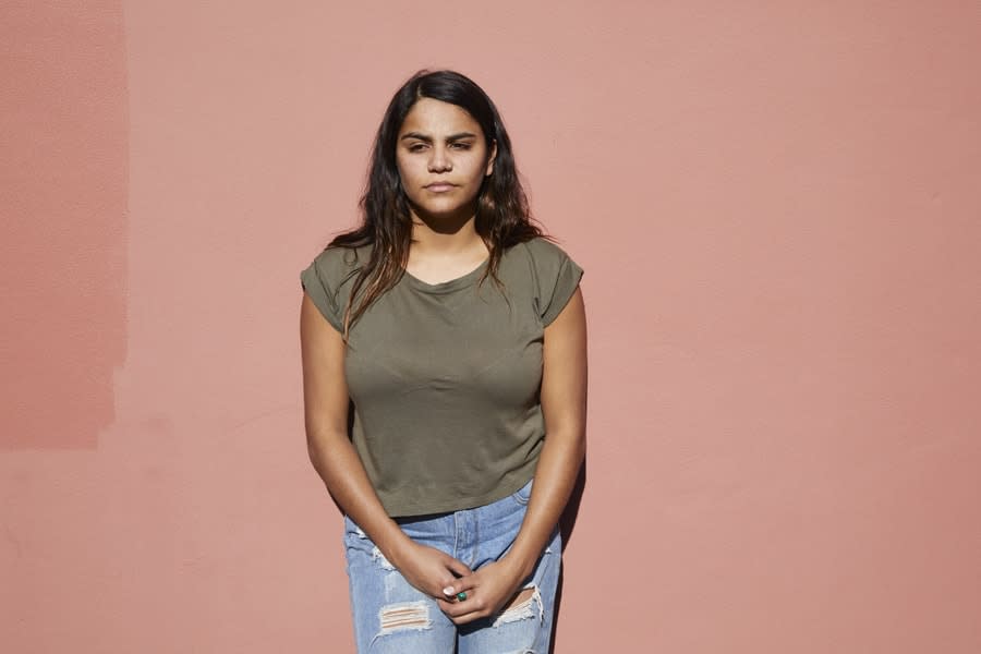 Young person standing in front of a pink wall. 