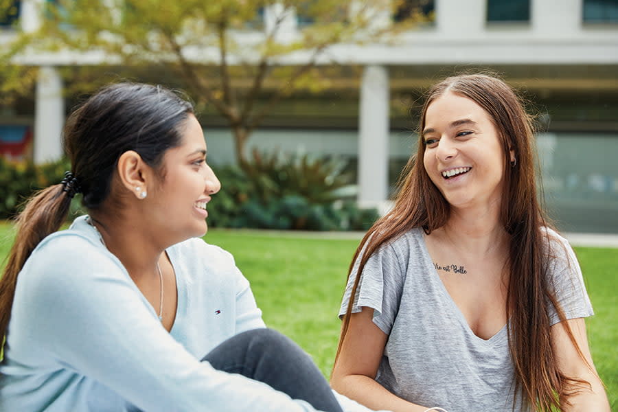 Image of two smiling teen girls sitting together in a park.