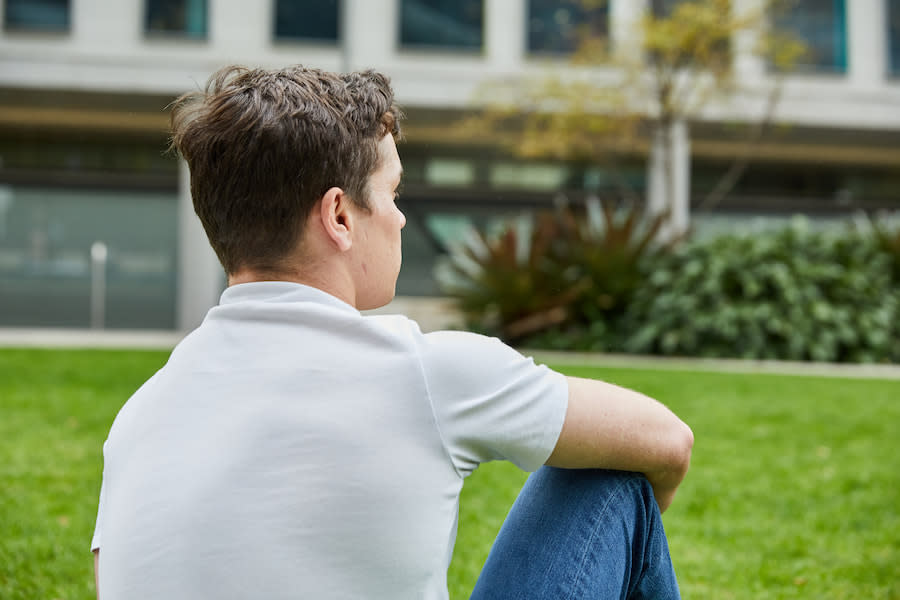 Image of a teen boy sitting outside. He has his back to the camera and is looking out into the distance.