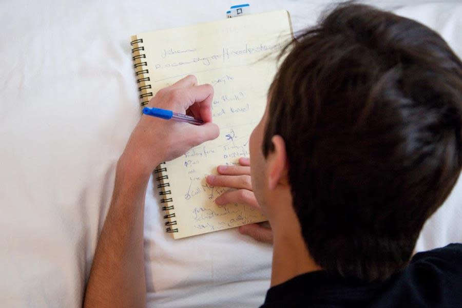 Aerial view of lefthanded guy on bed writing in notebook