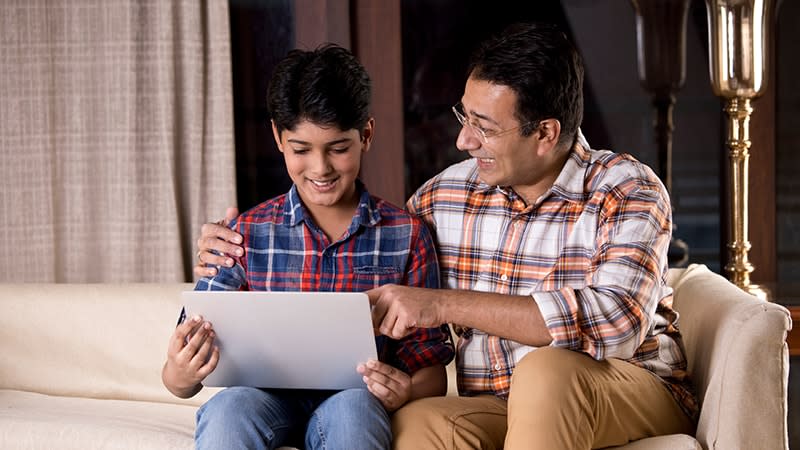 father and son sitting on couch looking at laptop