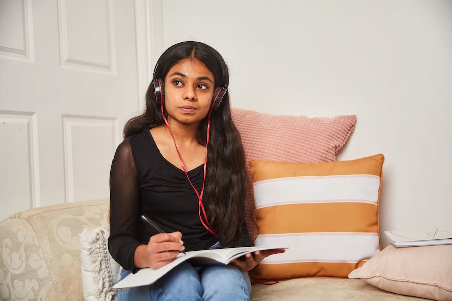 young woman sitting on a couch wearing headphones looking into the distance