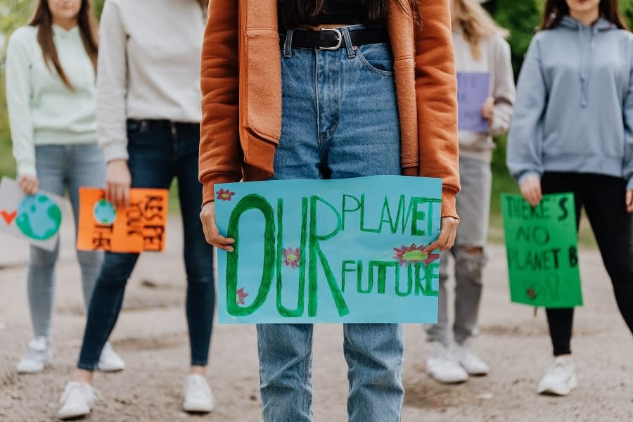 Teen in crowd of people holding protest sign that reads 'Our Planet Our Future'