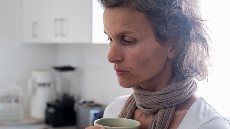 Pensive middle aged woman holding a cup of tea in kitchen