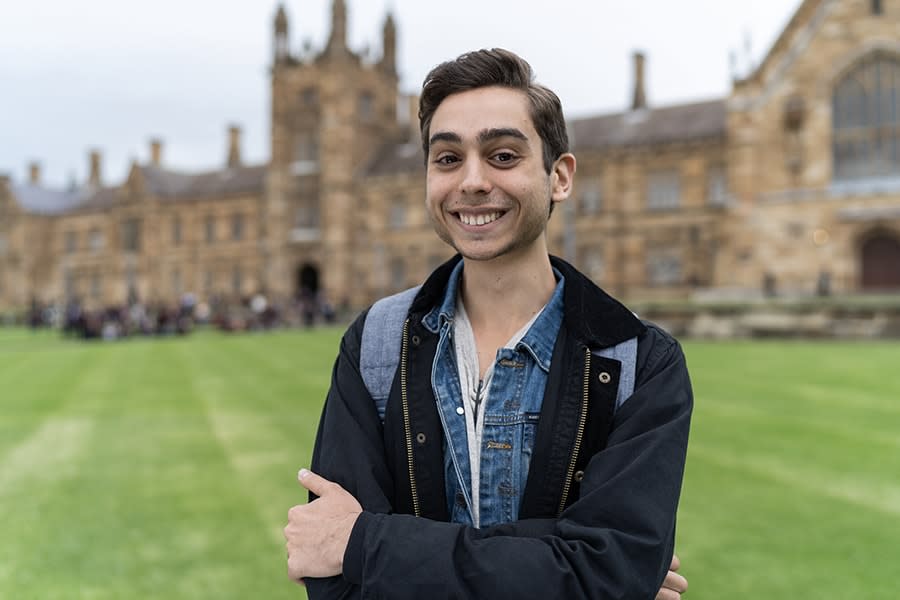 Danny boy in casual wear smiling with university building and courtyard behind him