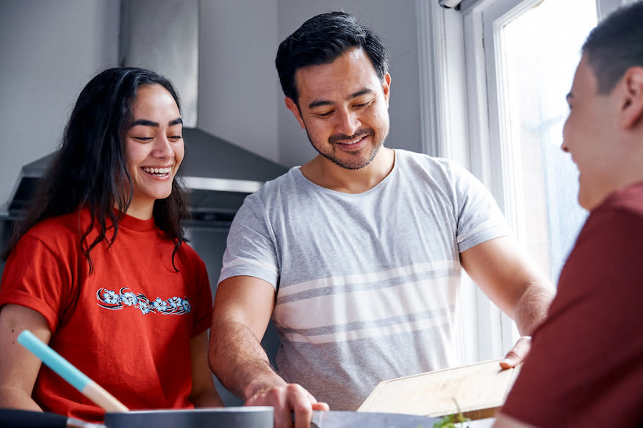 Image of a teenage girl smiling with dad and another teenager in a kitchen.