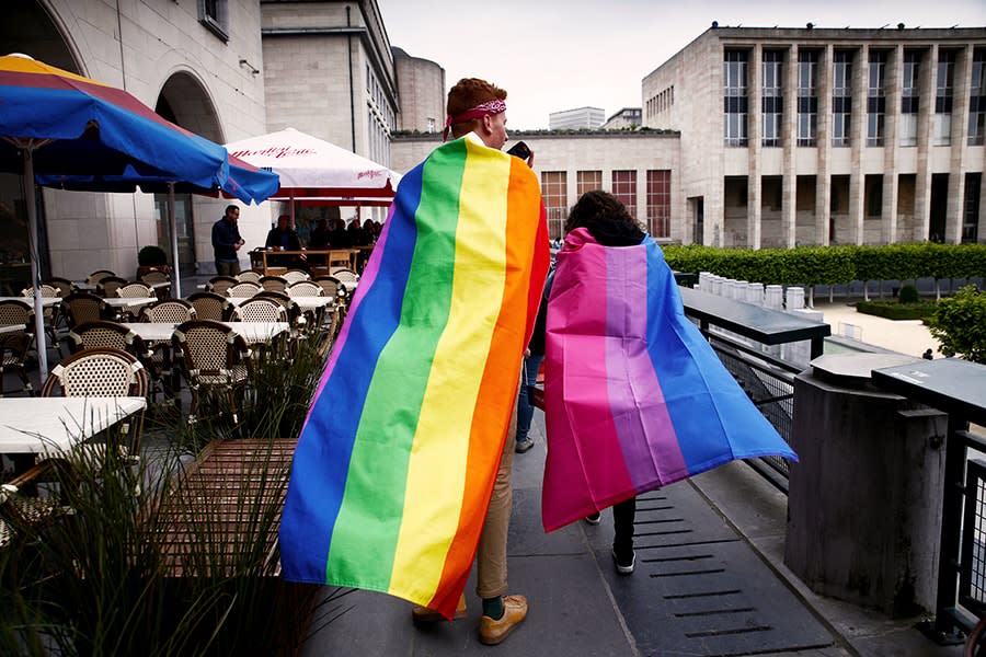 a man wearing a rainbow lgbtqi flag and a woman wearing a bisexual pink purple blue flag walking