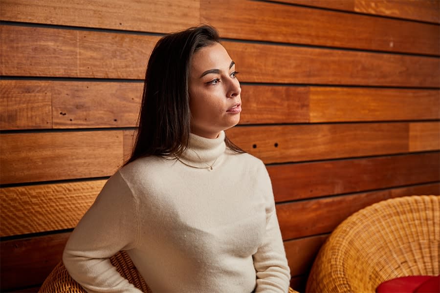 Young woman with long dark hair wearing a beige knitted jumper looks pensive