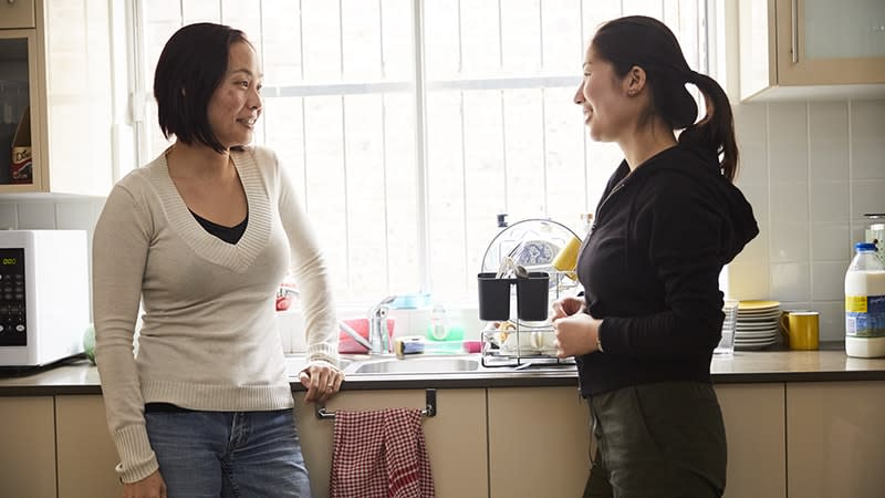 a woman and teenager stand in a kitchen talking