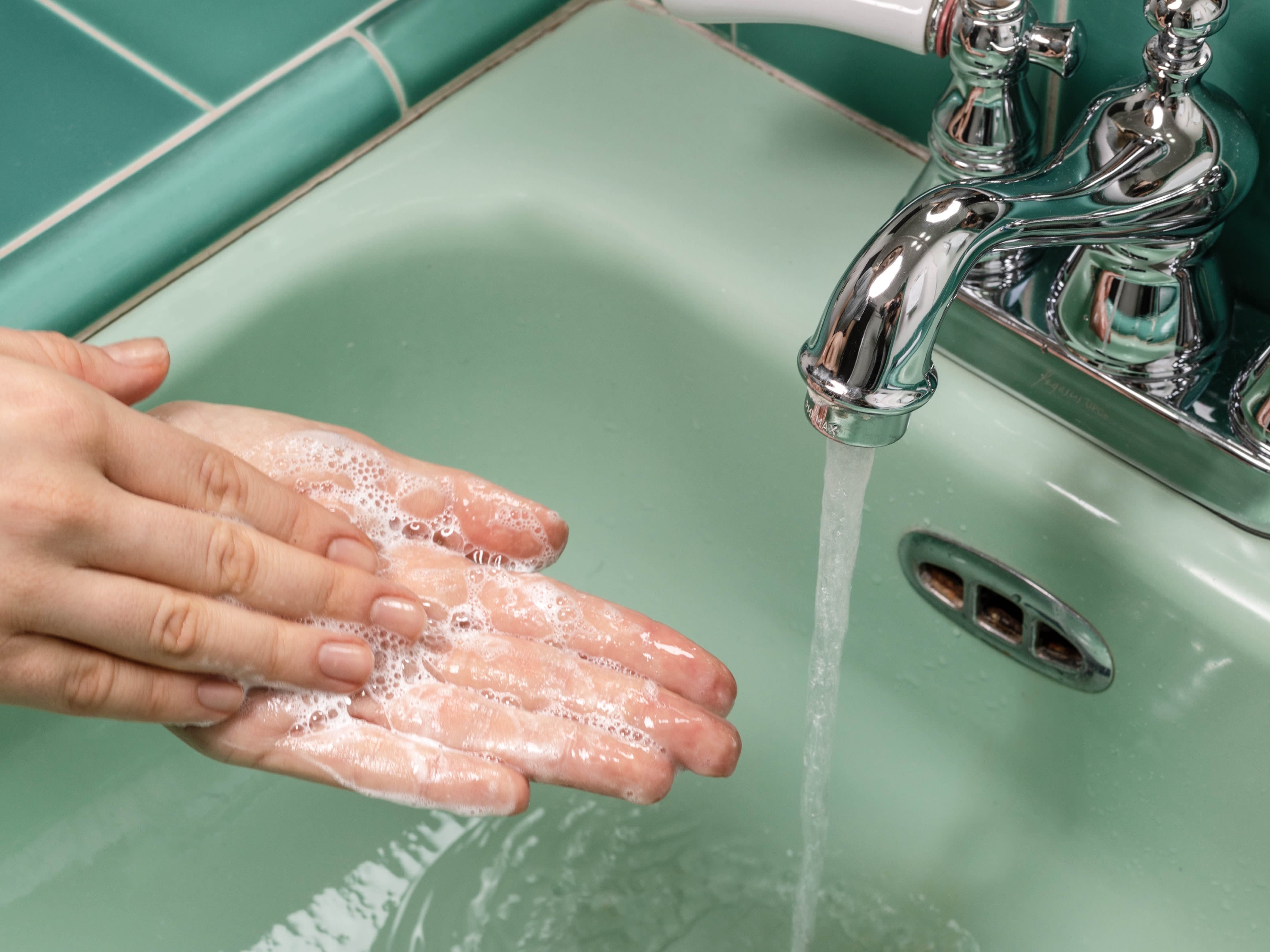 Woman washing her hands with a handwash in a green sink with the water running.