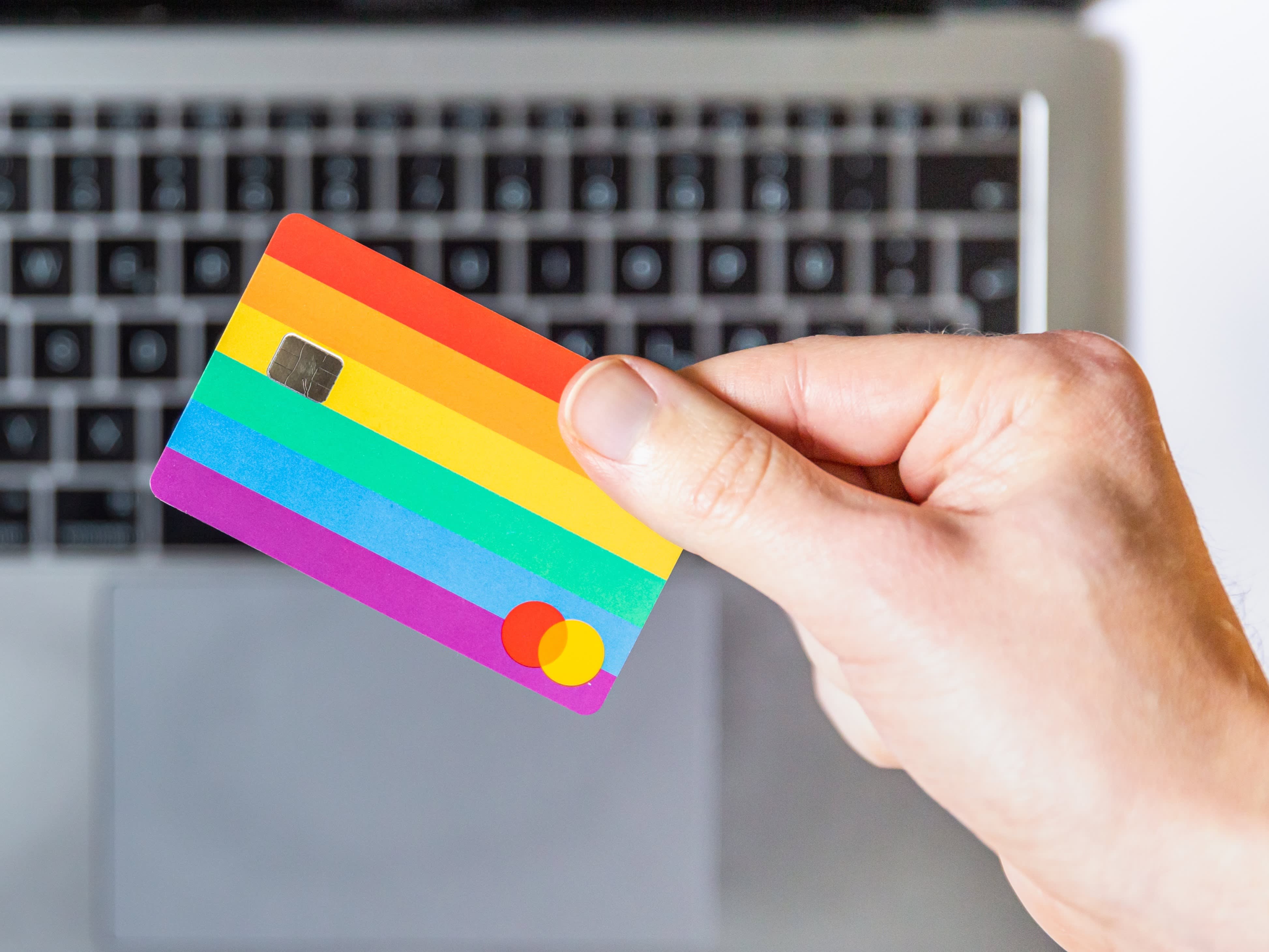 hand holding rainbow credit card above laptop