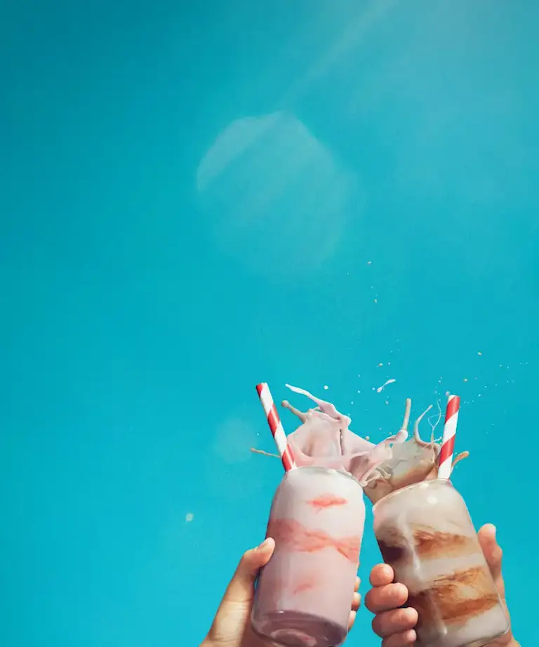 A strawberry milkshake and chocolate milkshake cheers against a blue sky background