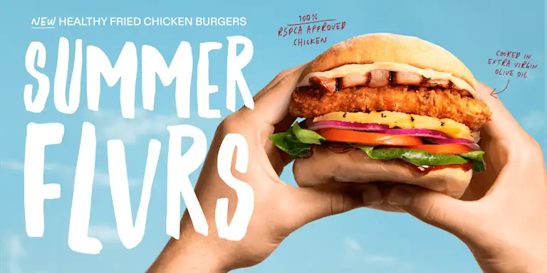 Two hands hold a healthy fried chicken burger against a bright blue sky. The burger features crispy fried chicken, fresh lettuce, tomato, onion, and sauce in a toasted bun. Large white text reads ‘Summer Flvrs’, with small notes highlighting ‘100% RSPCA Approved Chicken’ and ‘Crisp in extra virgin olive oil’.