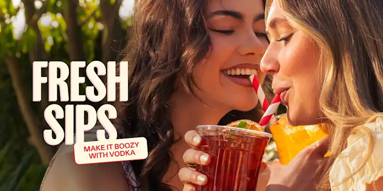 Two smiling women clink their iced summer drinks together and sip through striped straws in an outdoor setting. Text on the image reads “Fresh Sips” with a tag that says “Make it boozy with vodka.”