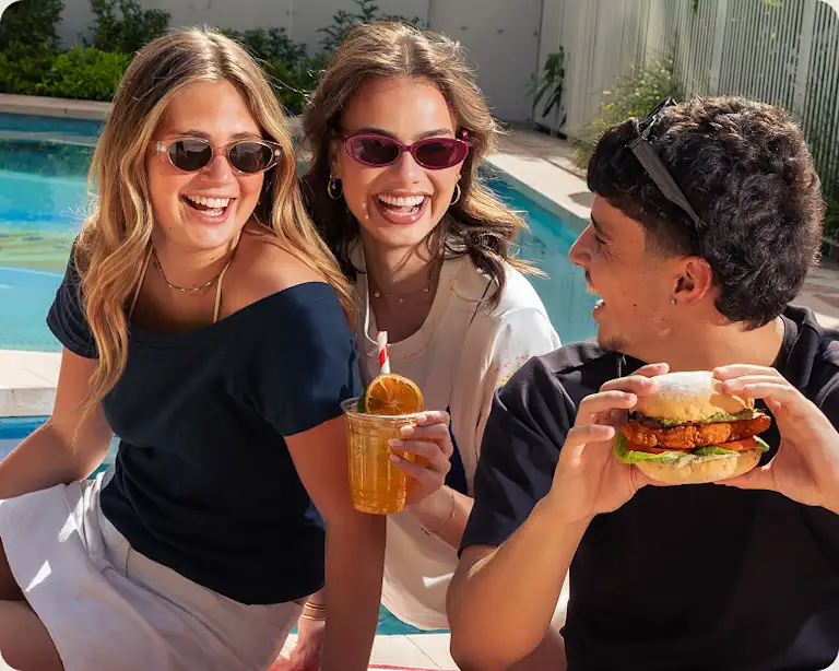 Friends by the pool enjoying healthy fried chicken burgers and drinks.