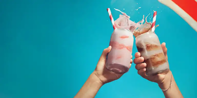 A strawberry milkshake and chocolate milkshake cheers against a blue sky background