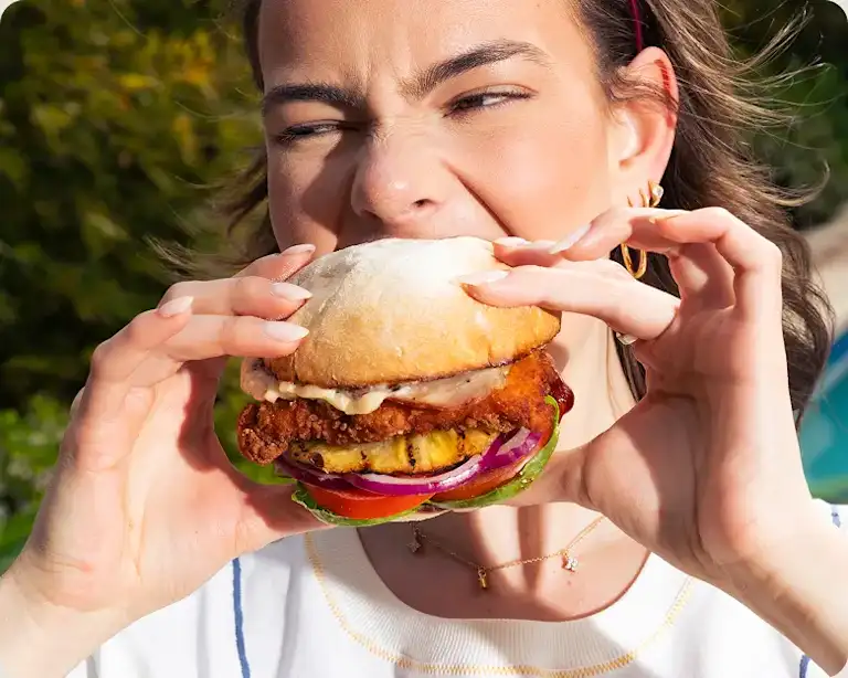 Person biting into a healthy fried chicken burger outdoors.