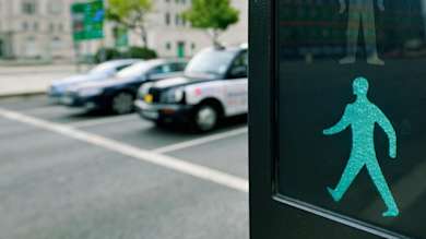 Closeup of green man signal at pedestrian crossing with cars waiting in the background
