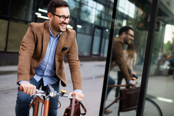 Bild: Froher Mann in braunem Sakko und Businesstasche fährt mit dem Rad zur Arbeit