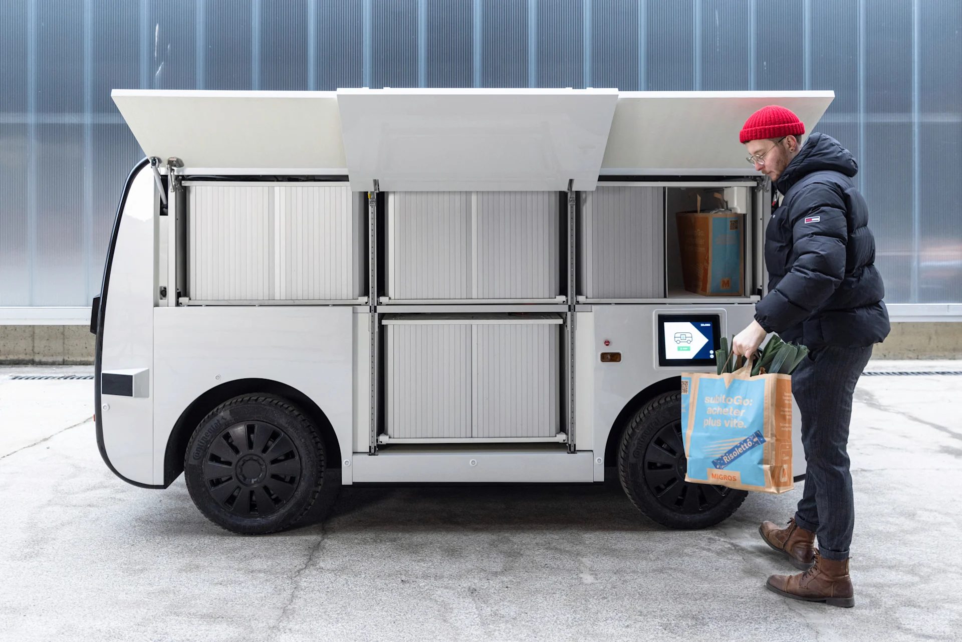 Dieses Robo-Auto könnte dir bald das Essen bringen Ein Mann nimmt eine Migros-Tasche aus dem selbstfahrenden Fahrzeug