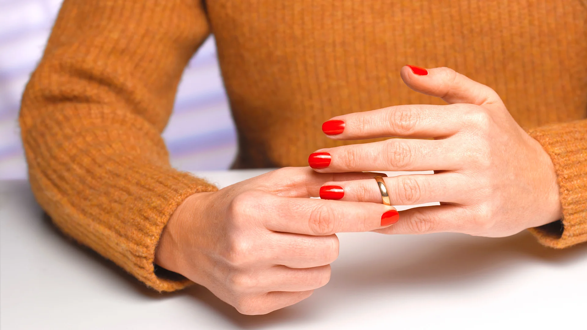 Divorzio e finanze: cosa devi sapere Una donna con un maglione arancione si toglie la fede dal dito.