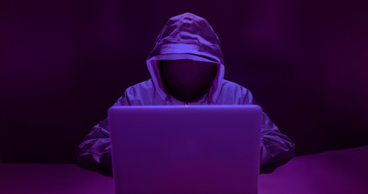 hooded figure sitting behind laptop with face not visible