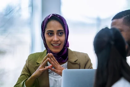 Woman wearing a head scarf talking with a multi-ethnic group of business people in an office boardroom. 