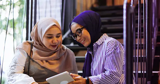 Two ladies sitting on stairs looking at a tablet