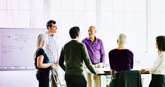 Team members standing up engaged in conversation around table