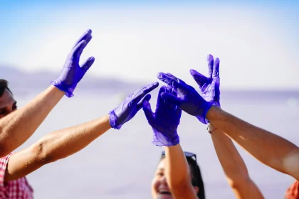 Group of friends collecting trash on beach early in the morning. Close up on their hands joined after successful job.