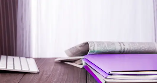 Keyboard, notebooks, and newspaper on wooden desk