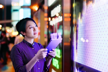 一名女商人在香港金融展板前查看平板电脑上的股市数据