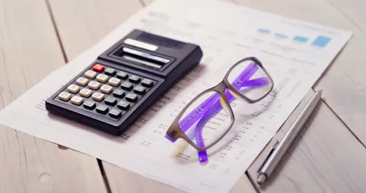 Calculator, pen, eyeglasses and tax forms on wooden table